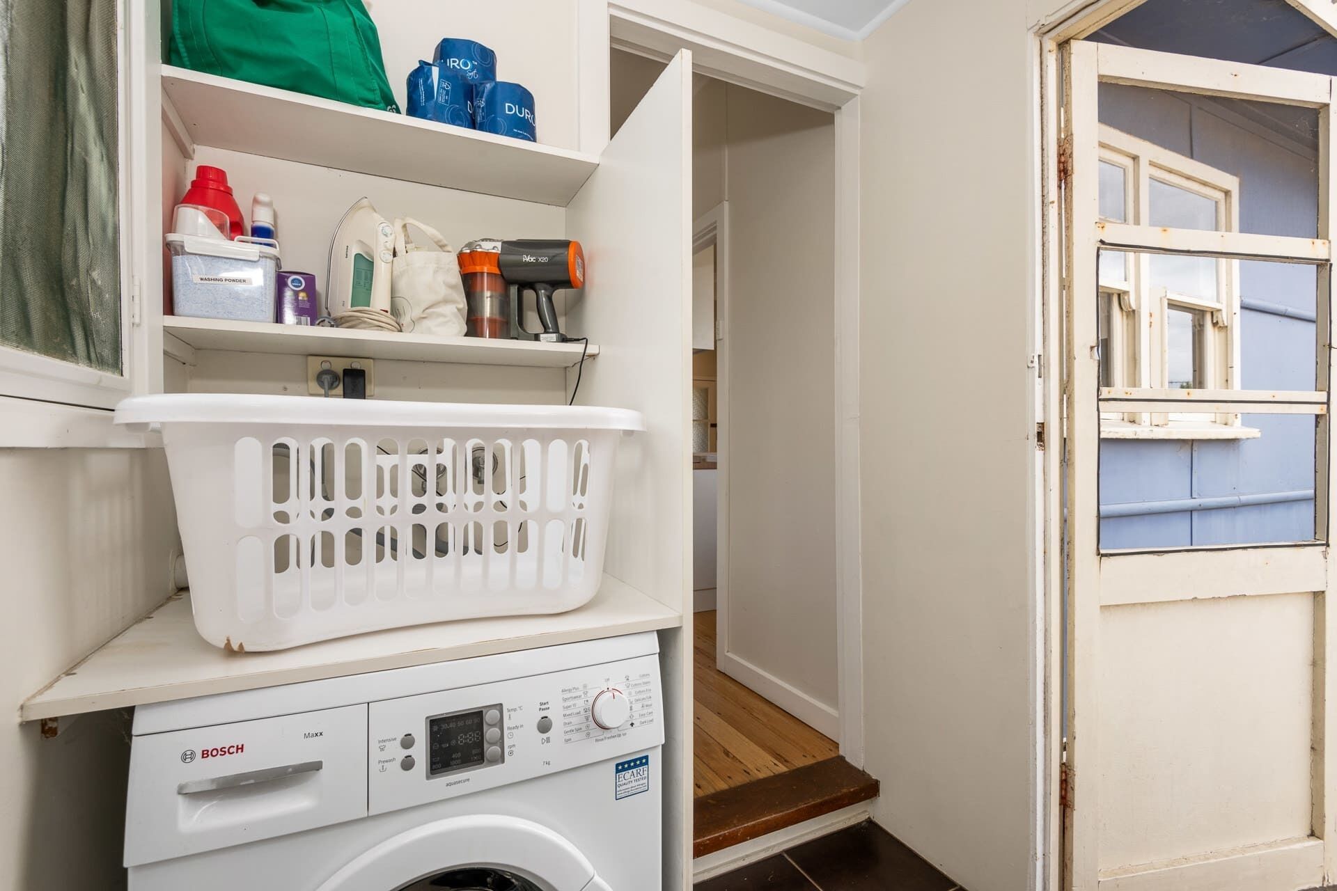 Een wasserette met een Bosch wasmachine, een droogrek en planken met wasbenodigdheden.