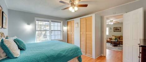A bedroom with a bed, a ceiling fan, a window, and a door leading to another room.