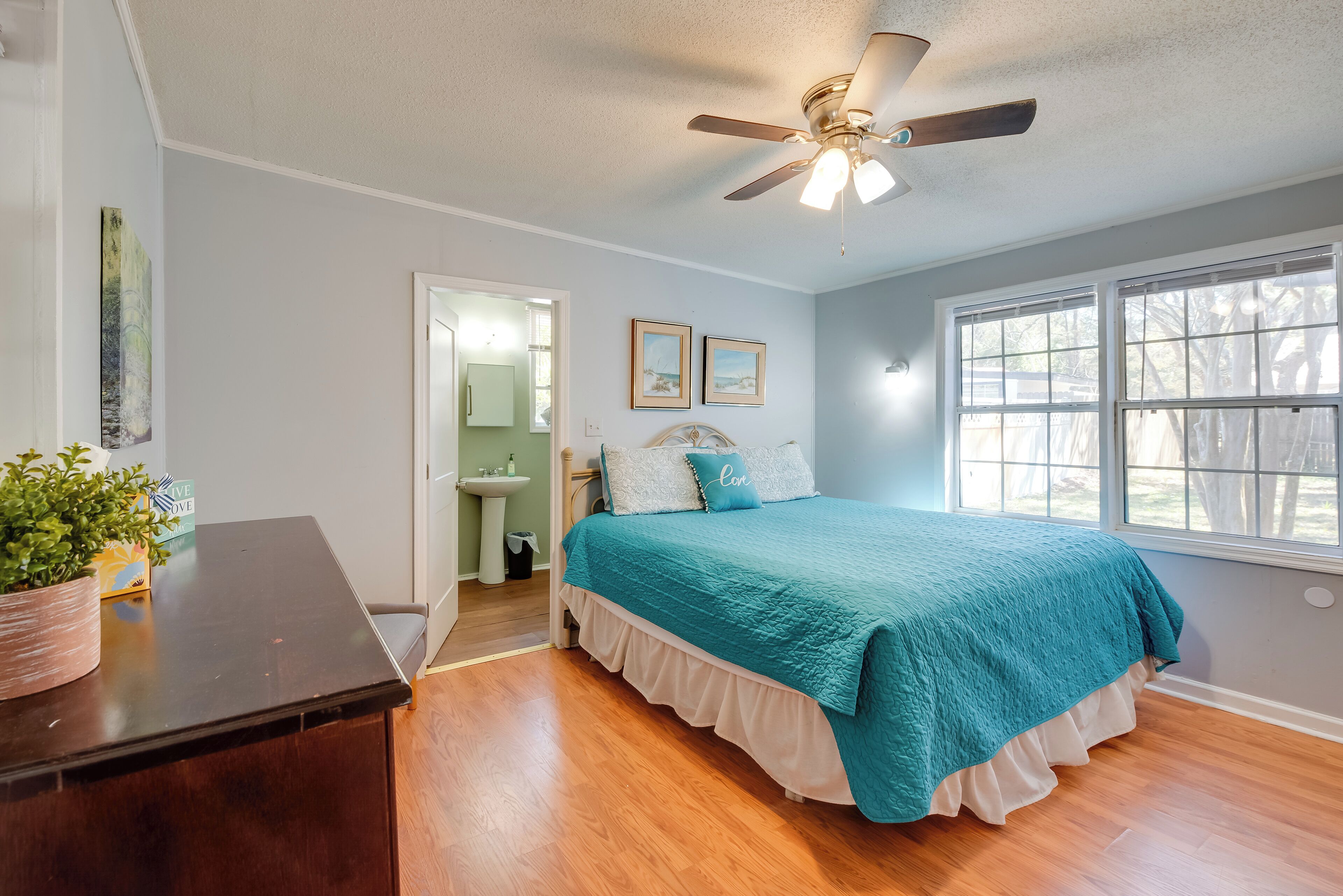 A bedroom with a bed, a ceiling fan, a window, and a plant on a dresser.