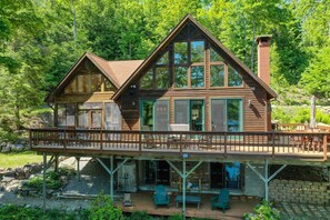 Une cabane en bois à deux étages, dotée d’un balcon, de grandes fenêtres et d’une cheminée.