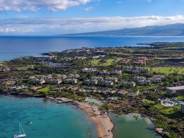 An aerial view of a coastal resort with multiple buildings, a beach, and clear blue waters.