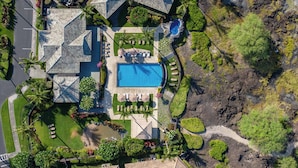 An aerial view of a resort with a swimming pool, multiple buildings with unique roofs, and lush landscaping. - Luxurious Kolea Kai Villa, Private Lanai w/ Ocean Views, Beach Club, Kona Coffee (Waikoloa Village)