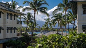 A coastal building with multiple balconies, surrounded by lush greenery and palm trees. - Luxurious Kolea Kai Villa, Private Lanai w/ Ocean Views, Beach Club, Kona Coffee (Waikoloa Village)