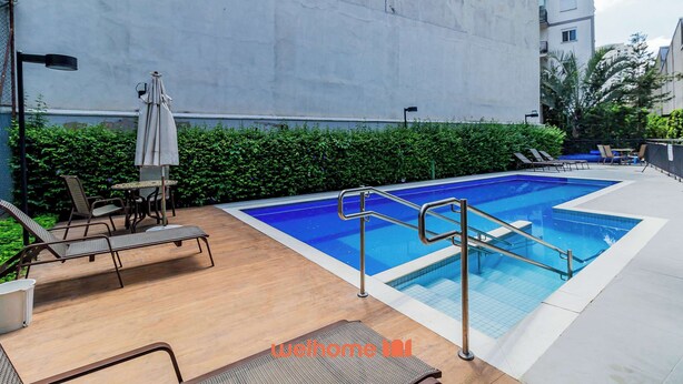 A rooftop pool area with lounge chairs and a table, surrounded by a low hedge and a building wall.