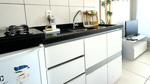 Una cocina moderna con armarios blancos, encimera negra, estufa integrada y un refrigerador pequeño.