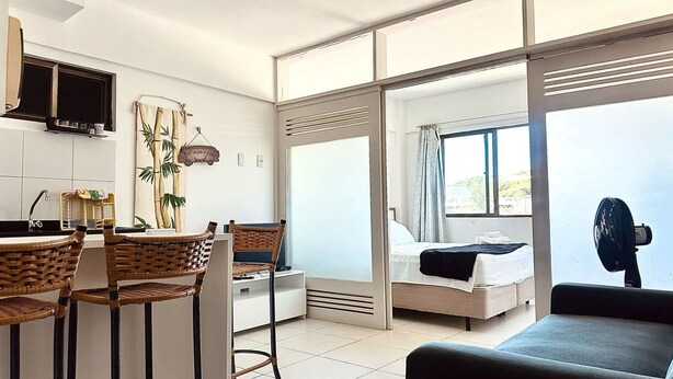 Una habitación moderna con cocina, una mesa de comedor con sillas, una cama y un ventanal grande.