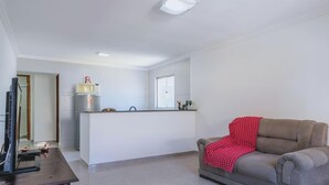 A living room with a sofa and a piano, a kitchen with a fridge and microwave, and a window. - Apartamento no Rio próximo à Lagoa da Tijuca (Rio de Janeiro)