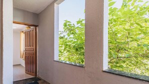 A hallway with a wooden door, a window with a view of green foliage, and a textured wall. - Apartamento no Rio próximo à Lagoa da Tijuca (Rio de Janeiro)