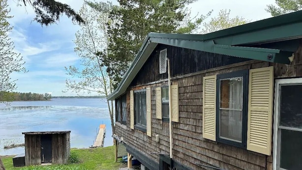 A wooden cabin with a view of a lake, a small shed, and a gravel path.