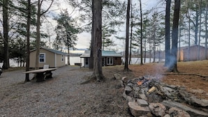 A cabin with a gravel ground, a fire pit, and a view of a lake.