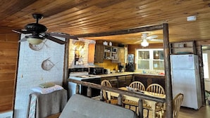 A rustic cabin interior with a kitchen area featuring wooden cabinets, a refrigerator, and a dining table with chairs.