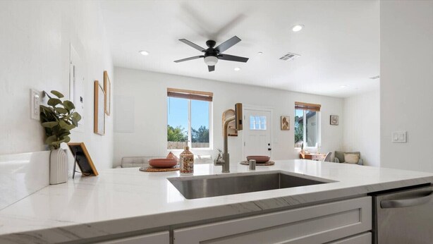 A modern kitchen with a large island, a ceiling fan, and a view of the outdoors.
