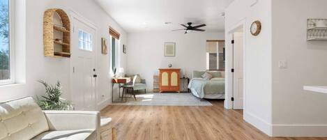 Un amplio espacio habitable con sofá, una mesa de centro de vidrio, un escritorio y una cama.