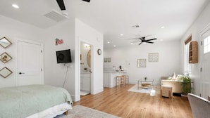 A modern bedroom with a bed, a TV, a ceiling fan, and a kitchen area.
