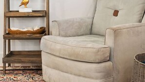 Una habitación con una alta estantería de madera, un sillón de color claro y una lámpara de pie.