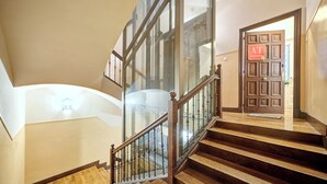 A staircase with wooden steps and glass railings, leading to a landing with a door marked "AT". - "Pamplona center suites" luxury Apartment city center (Pamplona)