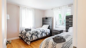 A bedroom with two beds, a wooden headboard, a nightstand, and a window with curtains. - Spacious 4 bedroom home with large yard (Wayland)