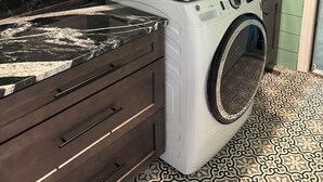 Ein kompakter Hauswirtschaftsraum mit nebeneinander gestapelten Waschmaschine und Trockner, einem dunklen Holzschrank und Fliesenboden mit Muster.