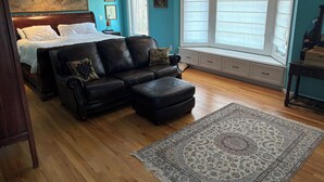 Ein Schlafzimmer mit einem Bett, einer schwarzen Ledersofa, einer Sitzbank an einem Fenster und einem großen Teppich.