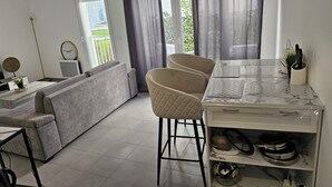 Una sala de estar moderna con un sofá gris, una mesa de comedor con sillas y una zona de cocina con encimera de mármol.