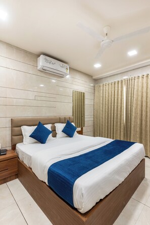A modern hotel room with a large bed, a nightstand, a ceiling fan, and an air conditioning unit. - Hotel Noble Inn (Ahmedabad)
