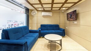 A modern waiting area with two blue sofas, a small round table, and a ceiling with recessed lighting. - Hotel Noble Inn (Ahmedabad)