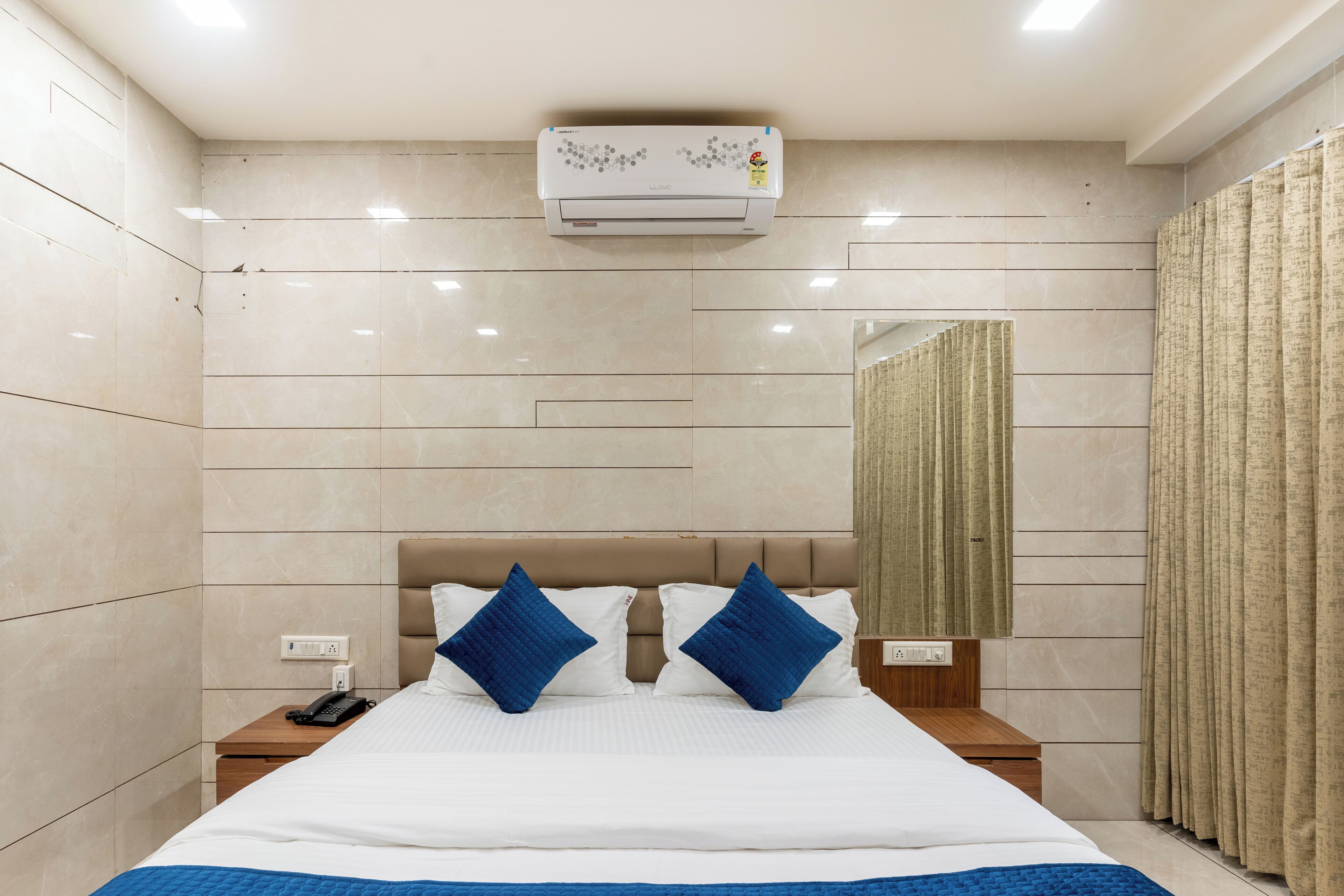 Habitación de hotel con una cama grande, dos mesitas de noche, aire acondicionado instalado en la pared y un espejo.