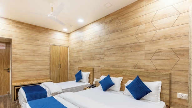 A hotel room with two beds, wooden panel walls, a ceiling fan, and a door with a sign. - Hotel Noble Inn (Ahmedabad)