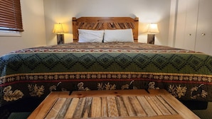 Un letto con una coperta a fantasia, due lampade ai lati del letto, una panca in legno e un armadio.