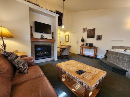A living room with a fireplace, a television, a coffee table, a sofa, and a bathroom with a bathtub.