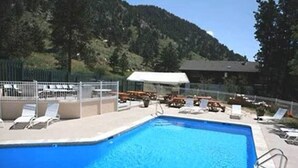Una piscina con lettini da relax e un'area recintata, circondata da alberi e un edificio sullo sfondo.