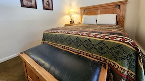 Een slaapkamer met een bed, een bankje, twee ingelijste foto’s aan de muur en een nachtkastje met een lamp.