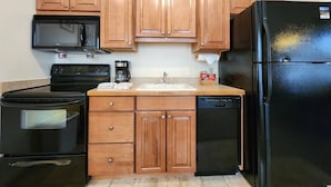 Une cuisine avec des meubles de rangement en bois, un réfrigérateur noir, un lave-vaisselle, une cuisinière et un four à micro-ondes.