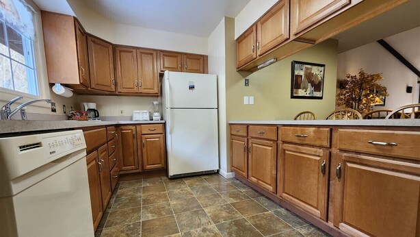 A kitchen with wooden cabinets, a white refrigerator, a dishwasher, and a tiled floor. - Fall River Overlook 202- With Seasonal Pool Access plus RMNP Entrance Close By! (Estes Park)