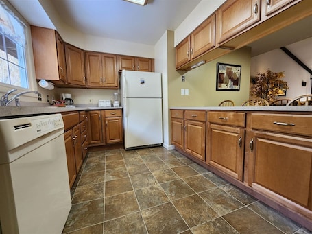 A kitchen with wooden cabinets, a white refrigerator, a dishwasher, and a tiled floor.