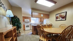 A dining area with a round table and chairs, a kitchen in the background, a clock on the wall, and a potted plant. - Fall River Overlook 202- With Seasonal Pool Access plus RMNP Entrance Close By! (Estes Park)