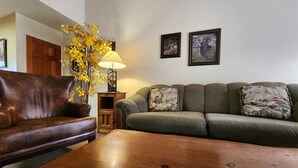A living room with a brown leather sofa, a green sofa with patterned cushions, a wooden coffee table, a floor lamp, and two framed pictures on the wall. - Fall River Overlook 202- With Seasonal Pool Access plus RMNP Entrance Close By! (Estes Park)