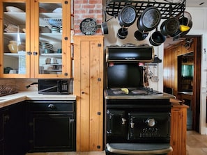 Una cocina con gabinetes de madera, microondas, estufa y ollas colgando.