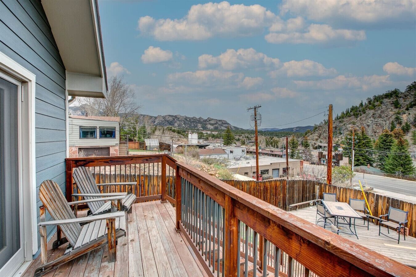 Une terrasse en bois avec des meubles d’extérieur, une vue sur une ville et des montagnes en arrière-plan.