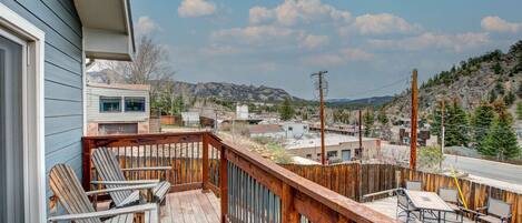 Une terrasse en bois avec des meubles d’extérieur, une vue sur une ville et des montagnes en arrière-plan.