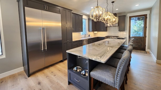 A modern kitchen with dark cabinets, stainless steel appliances, a marble island, and a bench seating area.