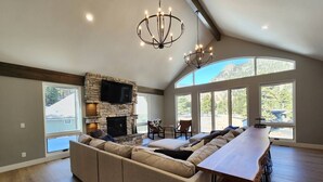 A spacious living area with a stone fireplace, a large L-shaped sofa, and a long dining table with bar stools.