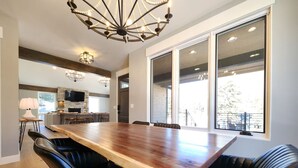 A modern dining area with a large wooden table, black leather chairs, and a chandelier.