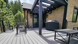 A wooden deck with outdoor furniture, a barbecue grill, and a covered seating area.