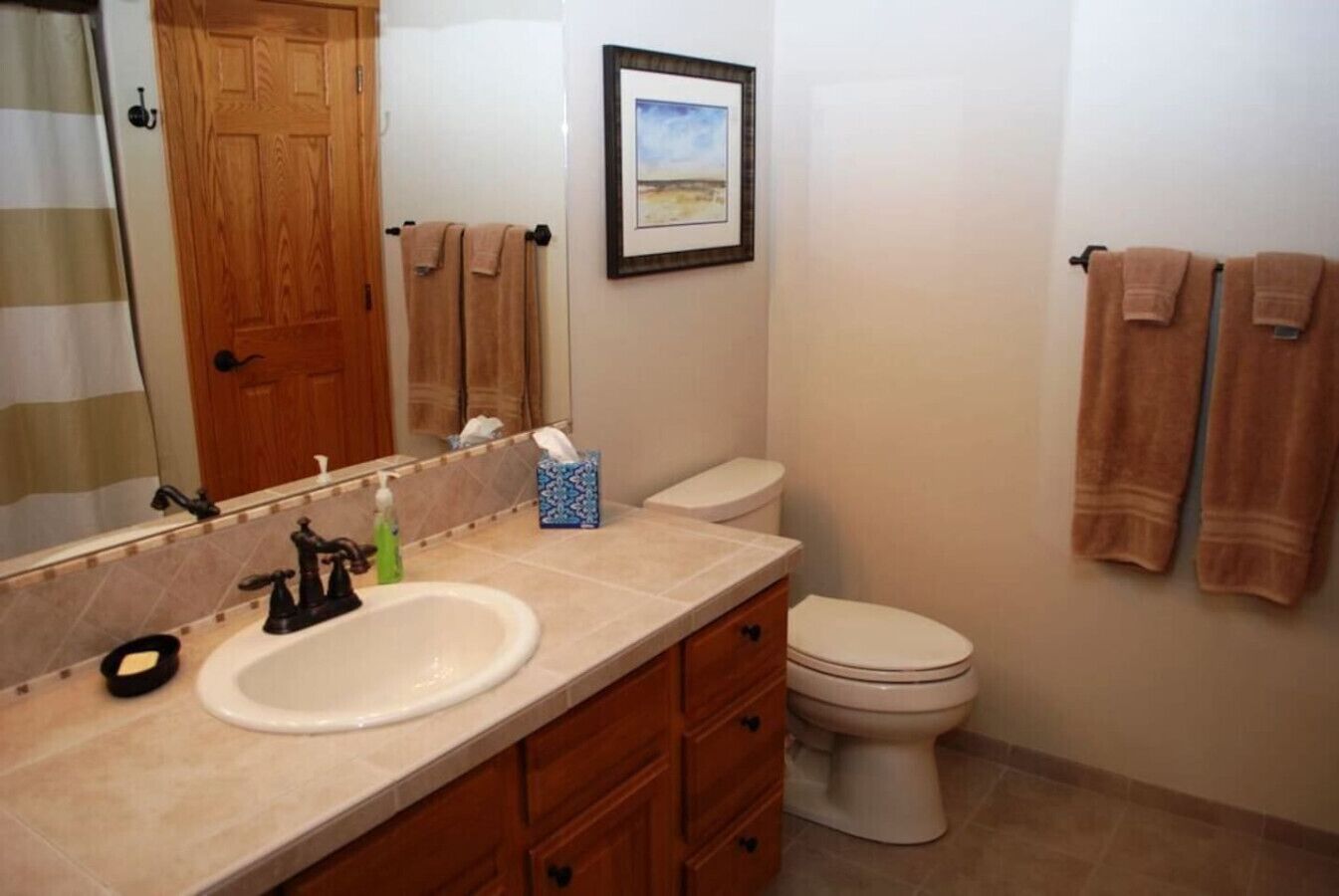 A bathroom with a wooden door, a sink with a mirror, a toilet, and towels hanging on the wall.