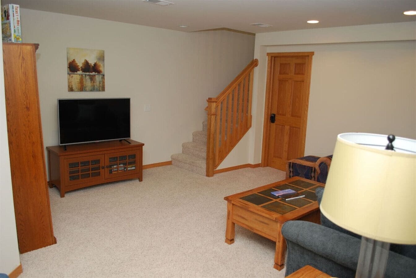 A living room with a TV on a wooden cabinet, a staircase, a coffee table, and a lamp.