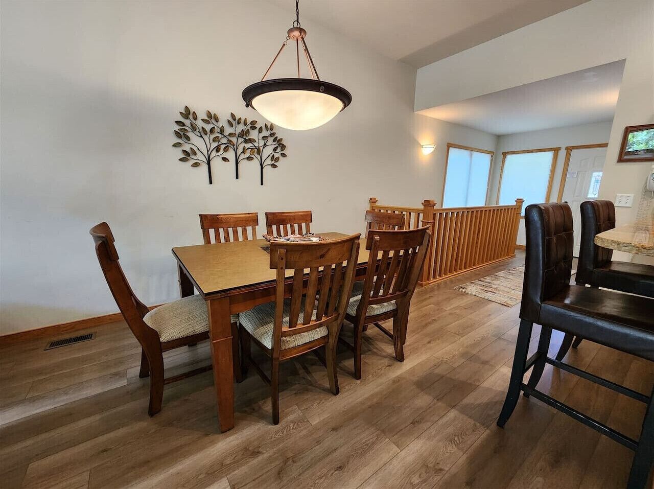 Een eetgedeelte met een houten tafel, stoelen, een hanglamp en een decoratief wandobject.