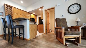 Una cocina con armarios de madera, un comedor con sillas, un reloj en la pared y un pasillo que conduce a otra habitación.