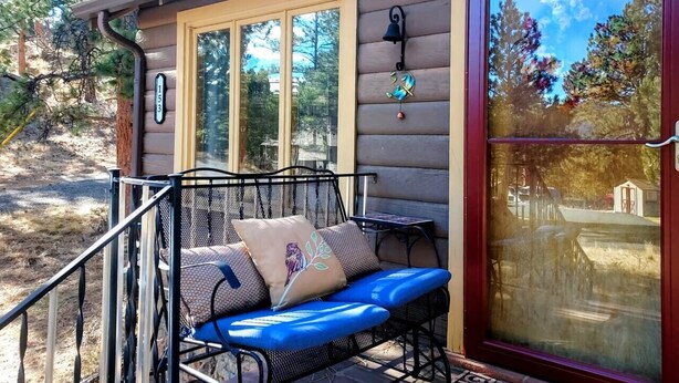 A log cabin with a porch, a metal bench with cushions, and a large glass door. - Bobcat`s Casita- Primal Serene Surroundings, Nearby Lake Estes, 9 and 18 hole golf, Stanley Hotel! (Estes Park)