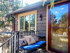 Une cabane en rondins avec un porche, un banc en métal doté de coussins et une grande porte en verre.